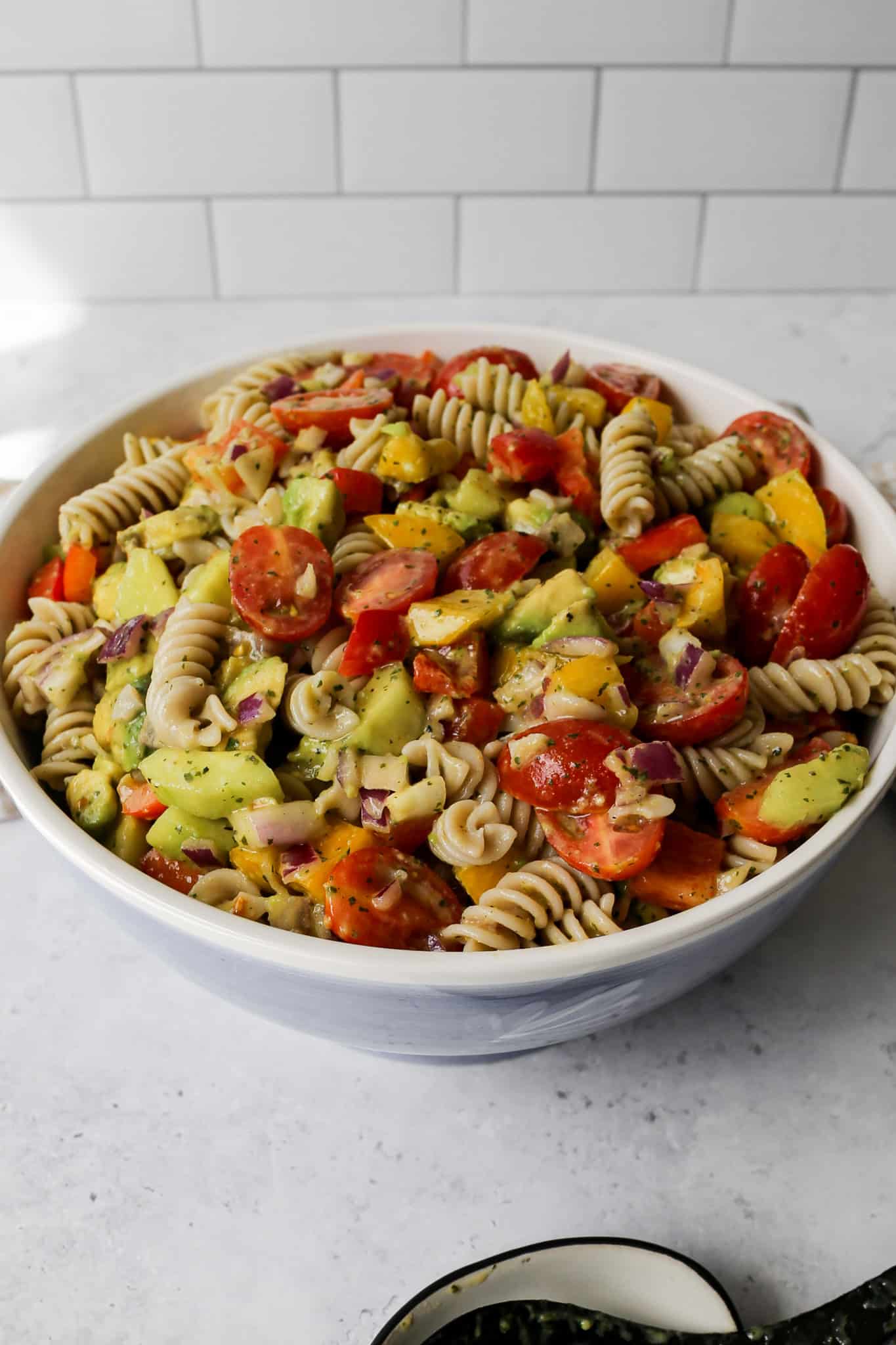 a serving bowl of gluten free lime cilantro pasta salad next to a serving spoon