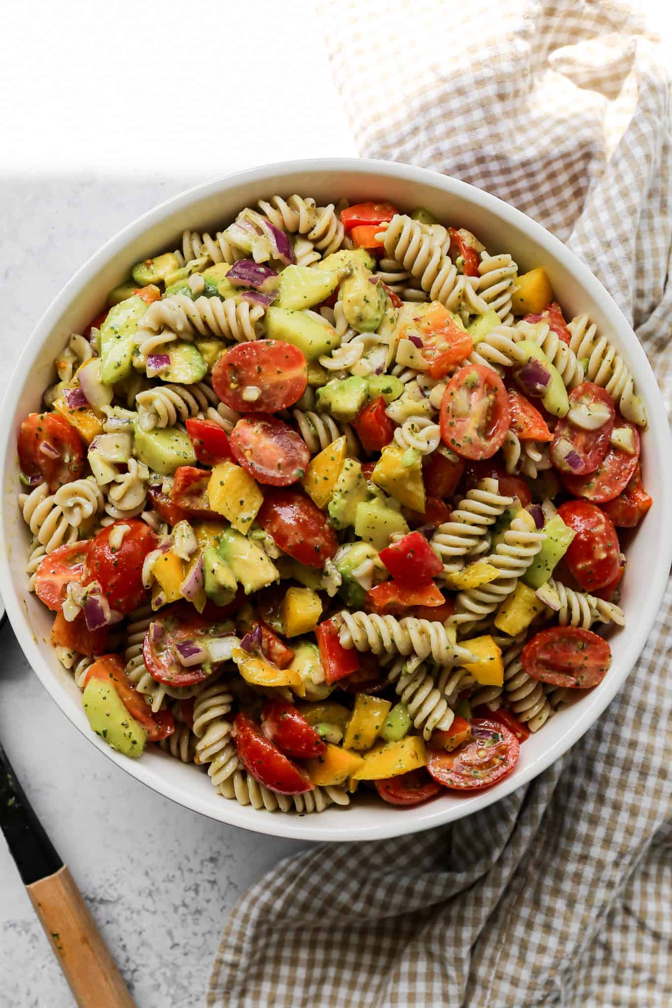 a serving bowl of gluten free lime cilantro pasta salad next to a serving spoon and a tan gingham kitchen towel