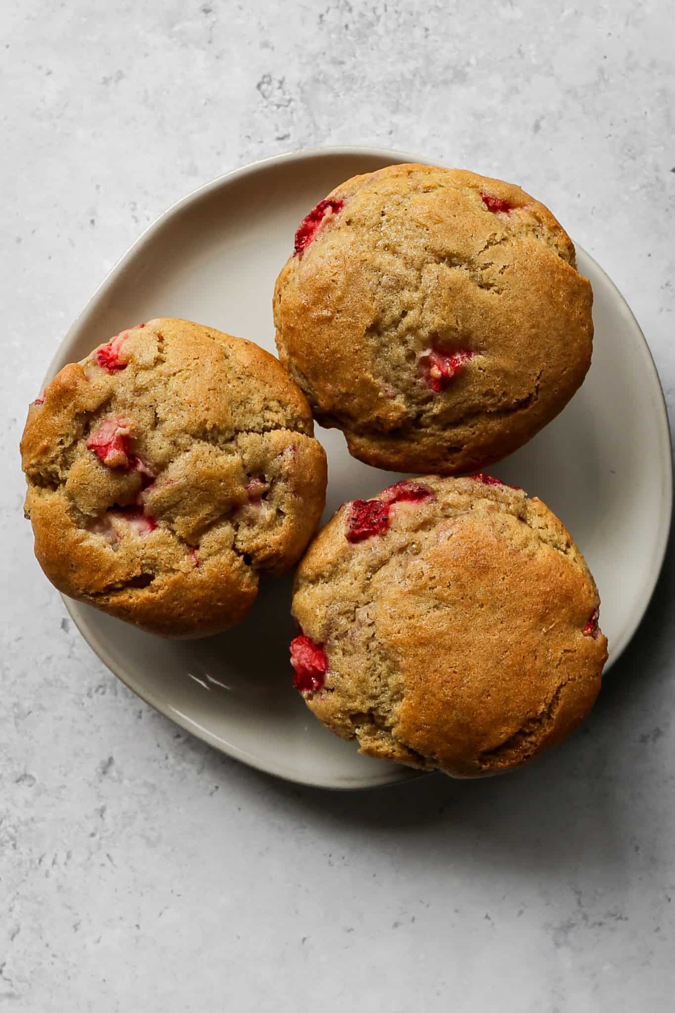 a cream colored small plate with three gluten free strawberry muffins on it
