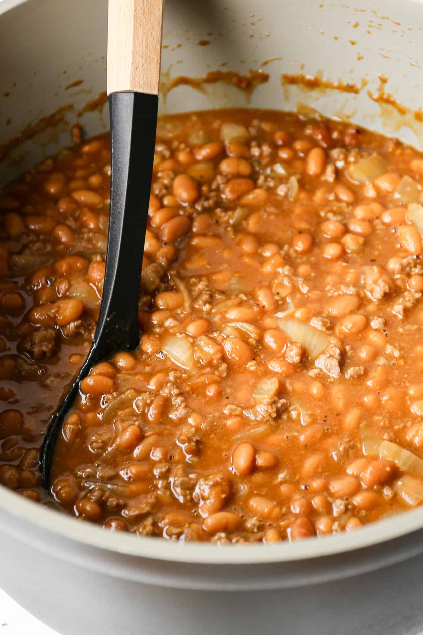 a dutch oven of gluten free baked beans with ground beef with a black spoon in them