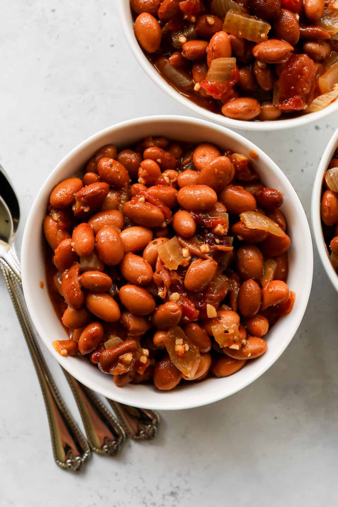three white bowls of gluten free slow cooker ranch style beans next to a tan gingham kitchen towel