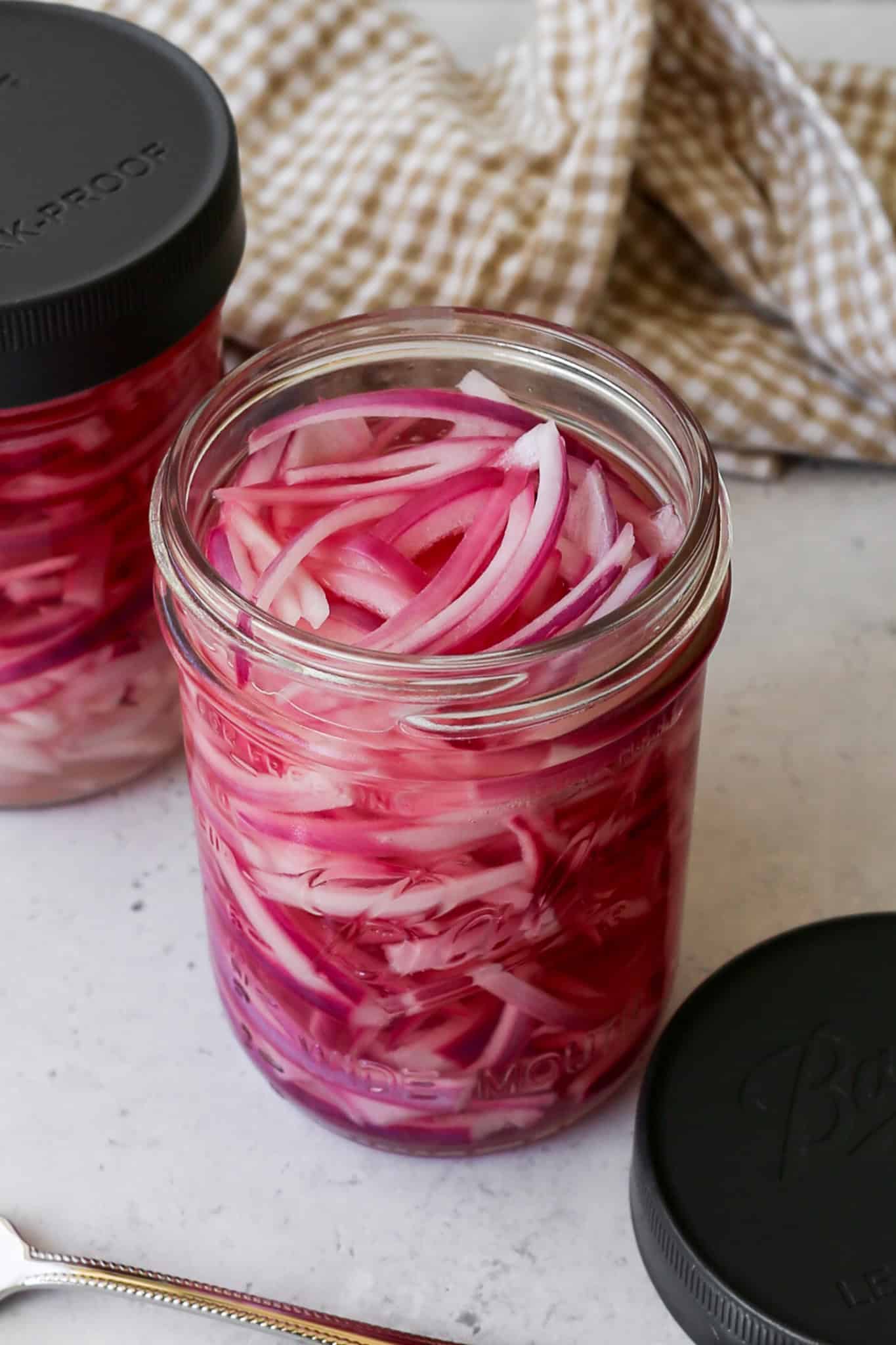 a sixteen ounce Ball canning jar of refrigerator quick pickled red onions next to a Ball sealable lid