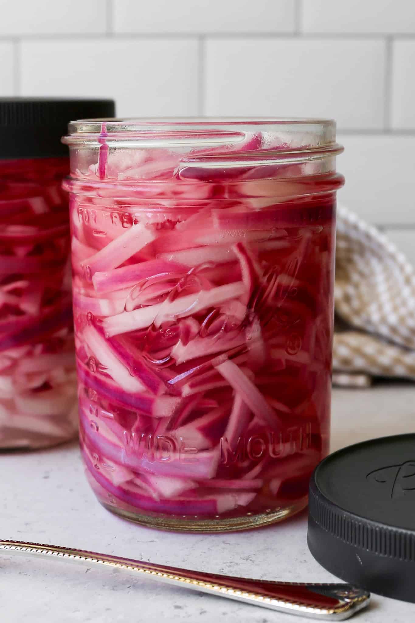 a sixteen ounce Ball canning jar of refrigerator quick pickled red onions next to a Ball sealable lid