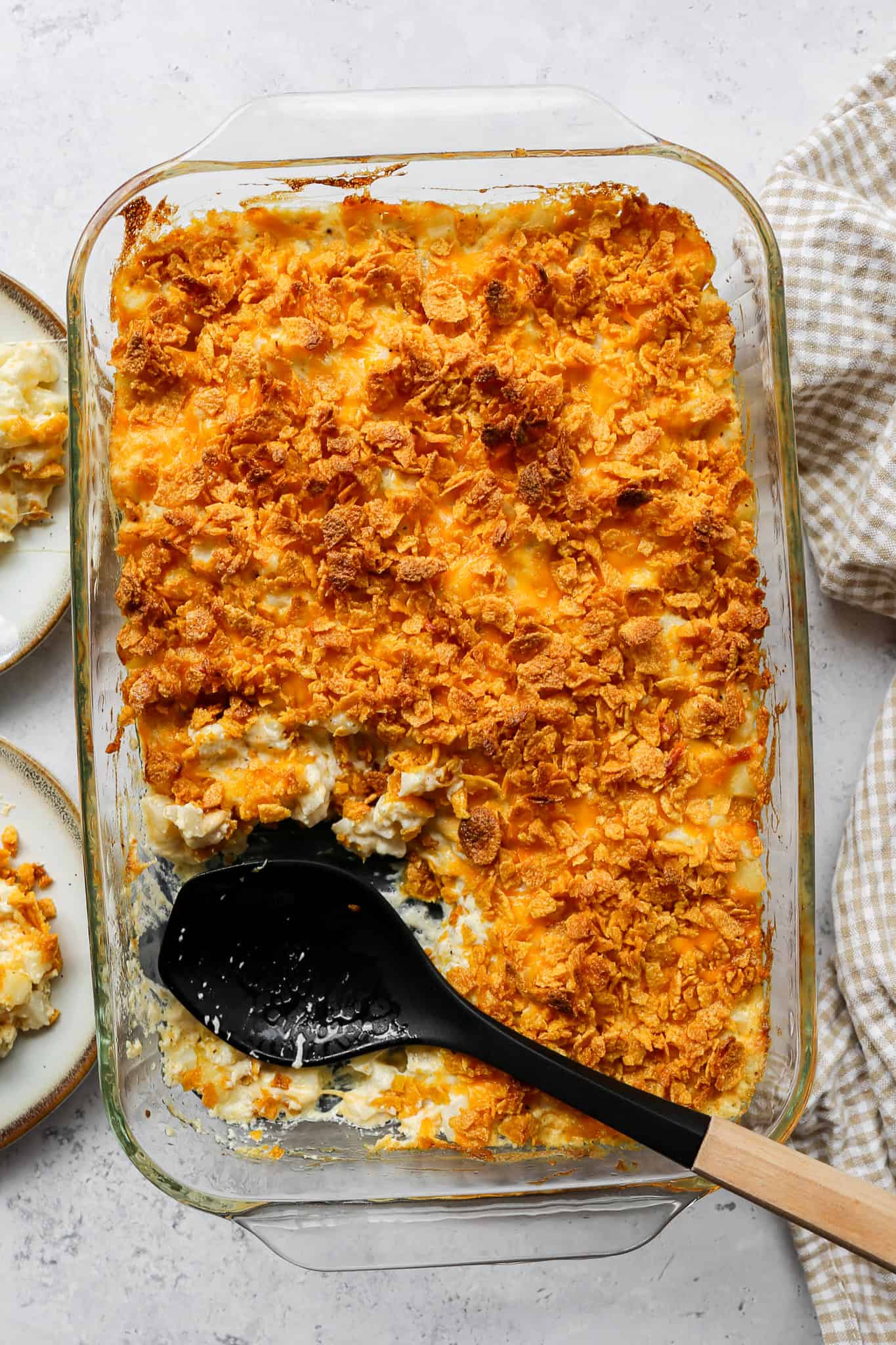 a clear glass 9x13 baking dish of gluten free funeral potatoes with a black wood handles serving spoon