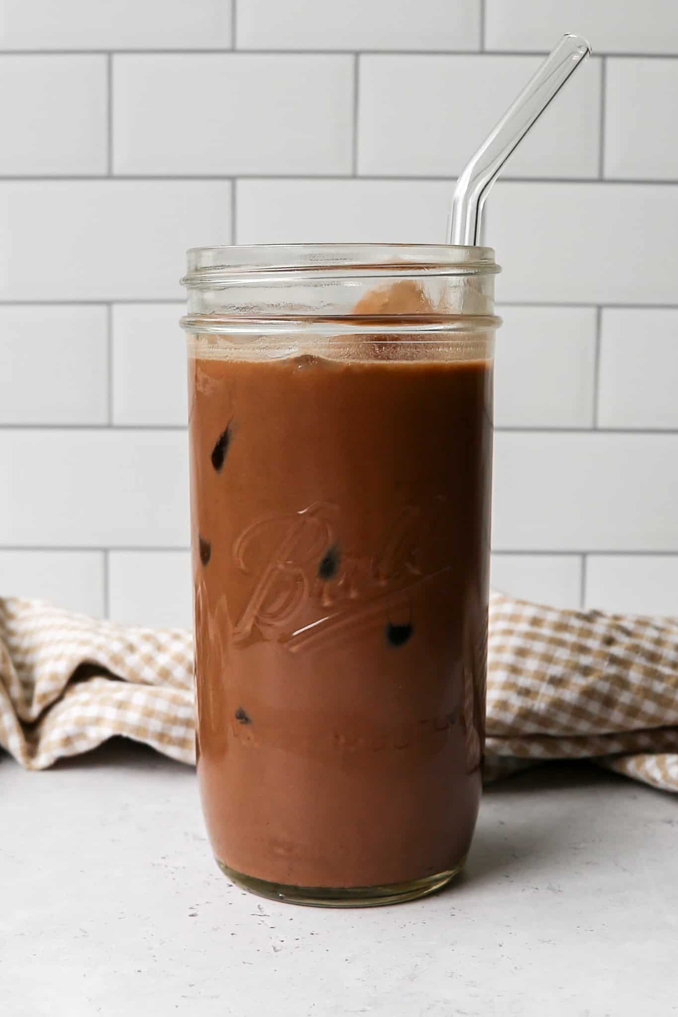 a clear glass Ball canning jar of iced mocha protein coffee over ice with a clear glass straw