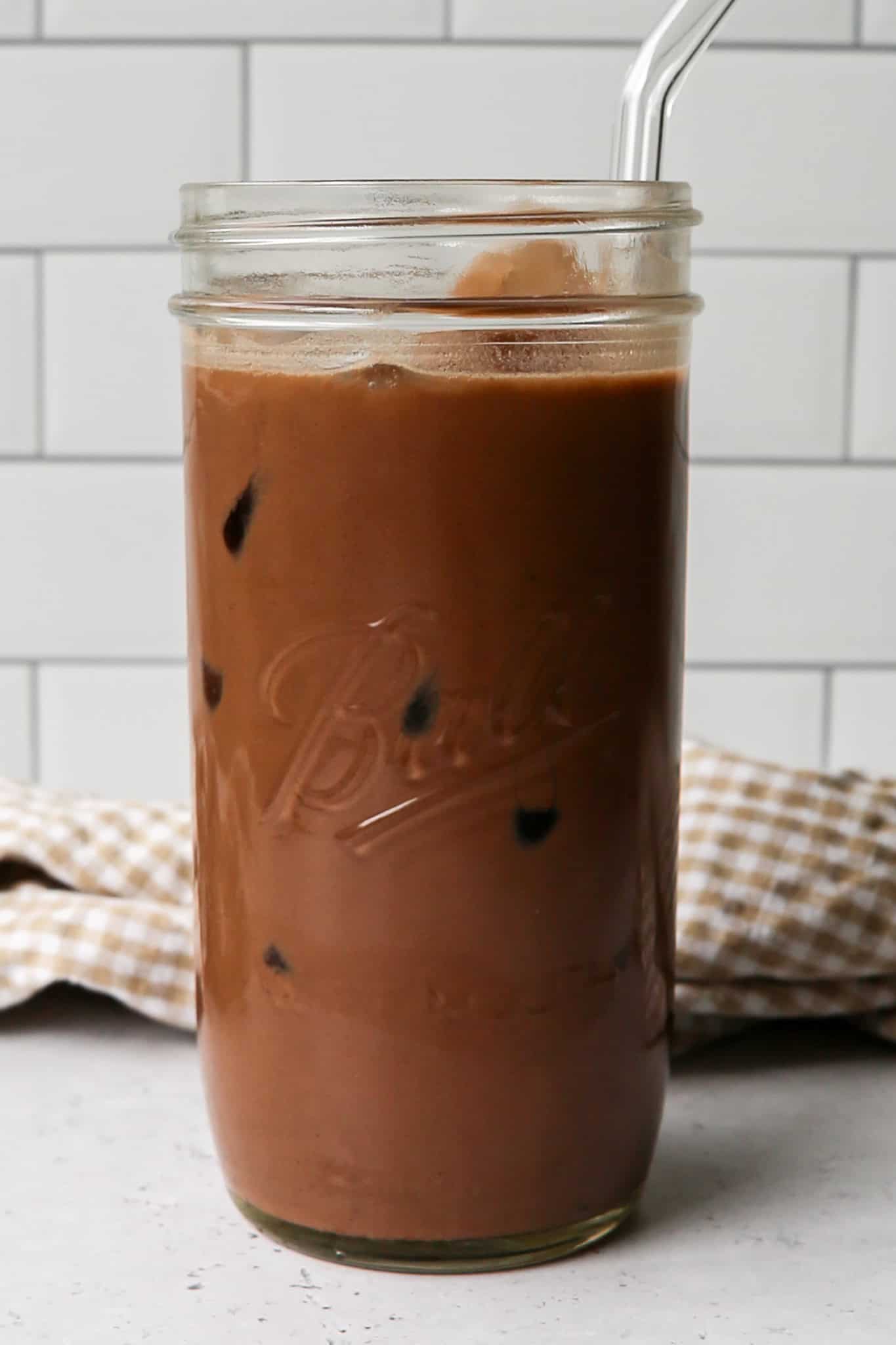 a clear glass Ball canning jar of iced mocha protein coffee over ice with a clear glass straw