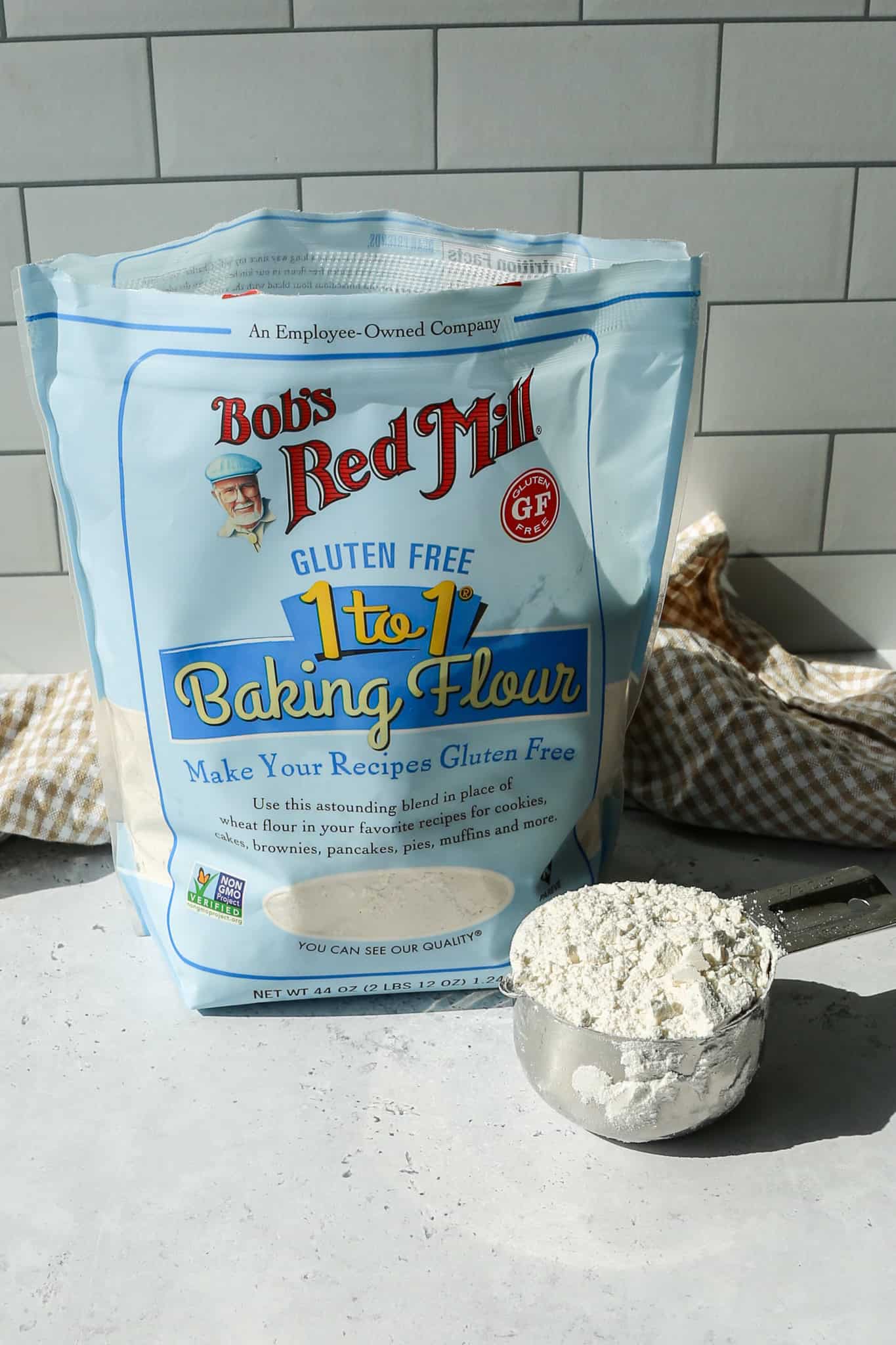 a bag of Bob's Red Mill Gluten Free 1 to 1 Baking Flour with a silver measuring cup of flour sitting next to the bag