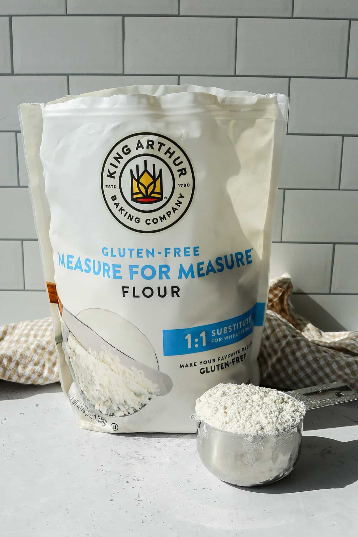 a bag of King Arthur Gluten Free Measure for Measure Flour with a silver measuring cup of flour sitting next to the bag
